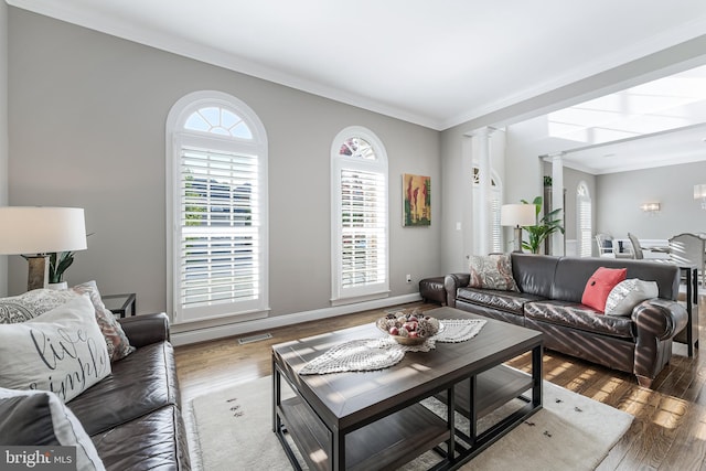 living room featuring visible vents, wood finished floors, baseboards, ornamental molding, and ornate columns