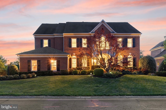 colonial home featuring brick siding, a lawn, and roof with shingles