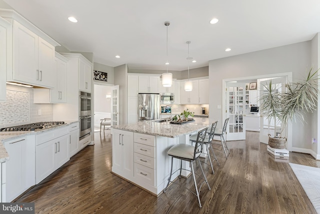 kitchen with a kitchen breakfast bar, a kitchen island, dark wood-style flooring, appliances with stainless steel finishes, and white cabinetry