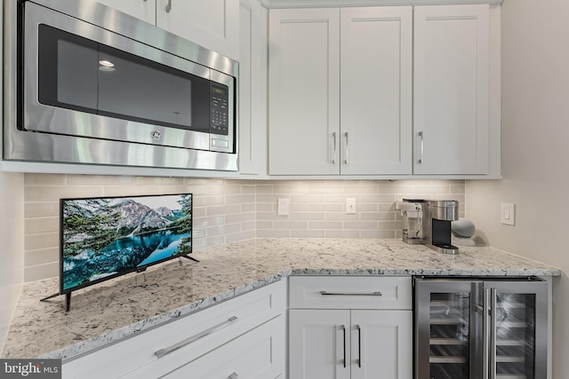 kitchen with white cabinets, stainless steel microwave, wine cooler, and tasteful backsplash