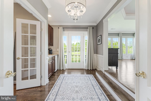 doorway featuring an inviting chandelier, ornamental molding, a wainscoted wall, and dark wood-style floors