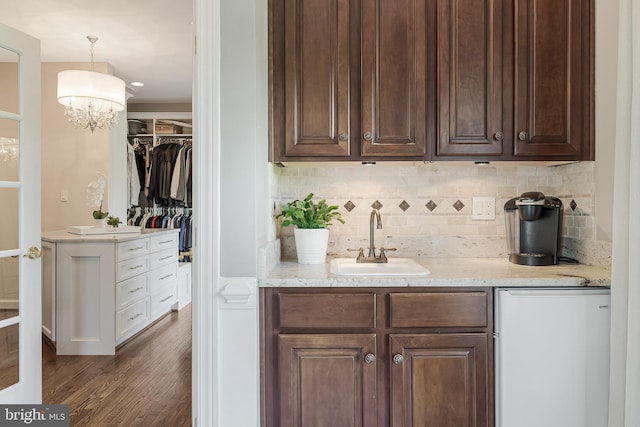 bar with decorative backsplash, dark wood-style flooring, hanging light fixtures, fridge, and a sink