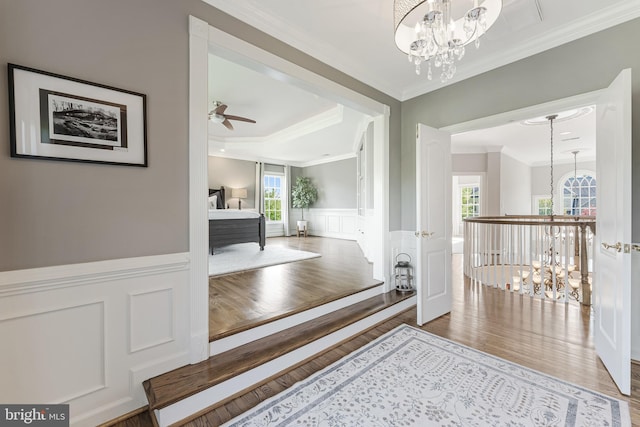 hall featuring a notable chandelier, ornamental molding, wood finished floors, and a decorative wall