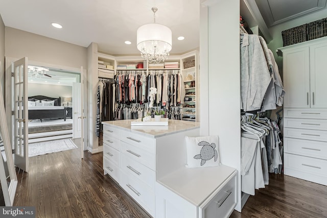 walk in closet with dark wood finished floors and ceiling fan with notable chandelier