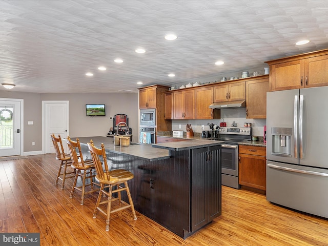 1996 Buck Mountain Rd, Bentonville, VA 22610 - kitchen featuring appliances with stainless steel finishes, dark countertops, under cabinet range hood, brown cabinetry, and recessed lighting