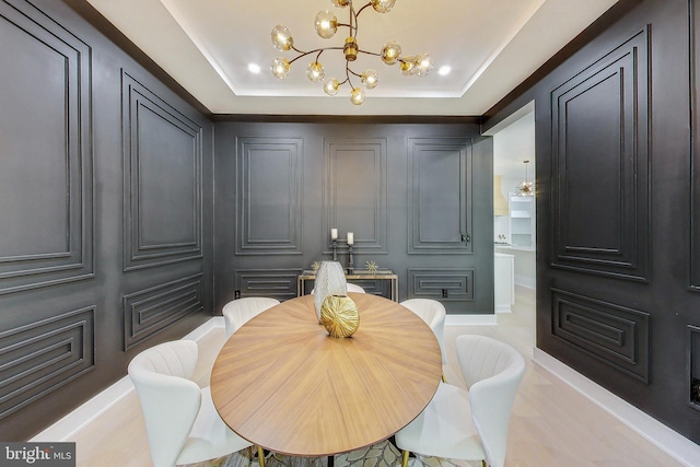 dining room with an inviting chandelier, a raised ceiling, and a decorative wall