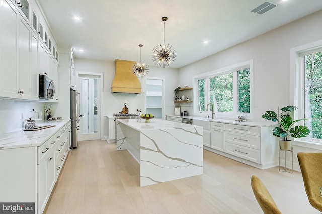 kitchen with visible vents, custom exhaust hood, light wood-type flooring, a center island, and appliances with stainless steel finishes
