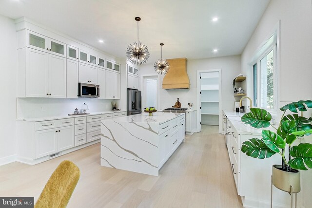 kitchen with appliances with stainless steel finishes, a center island, white cabinetry, custom range hood, and visible vents