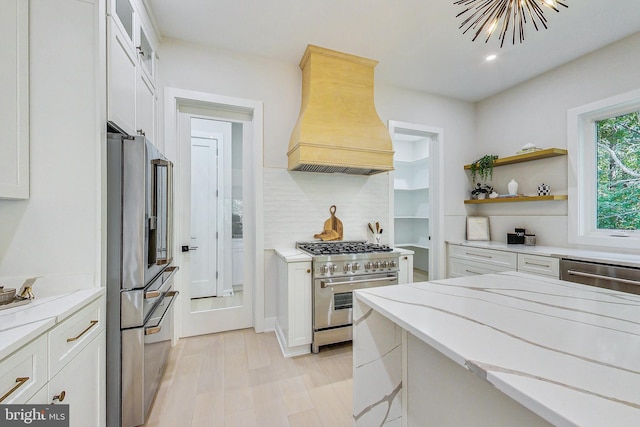 kitchen with white cabinetry, premium appliances, light stone countertops, and premium range hood