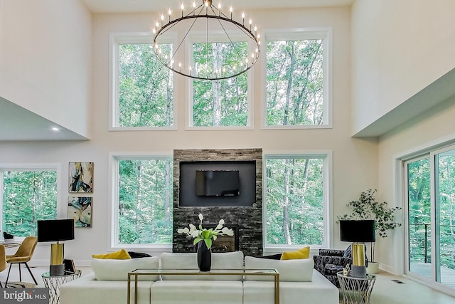 living area featuring a healthy amount of sunlight, a notable chandelier, a premium fireplace, and a towering ceiling