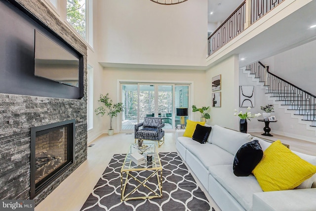 living area featuring a high ceiling, a stone fireplace, baseboards, wood finished floors, and stairway