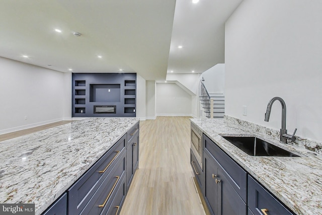 kitchen featuring built in features, light stone countertops, baseboards, light wood-type flooring, and a sink