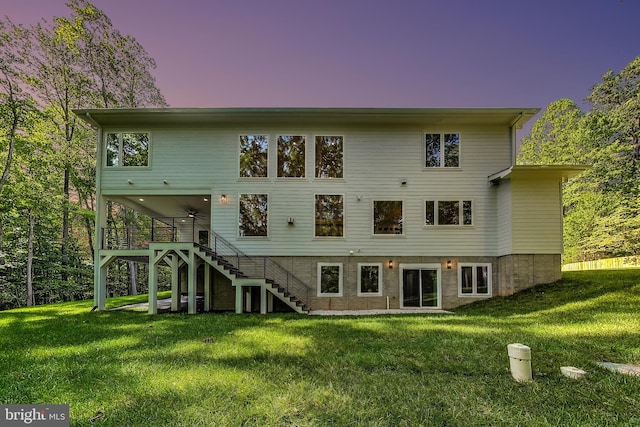 back of house with a lawn, a ceiling fan, and stairway