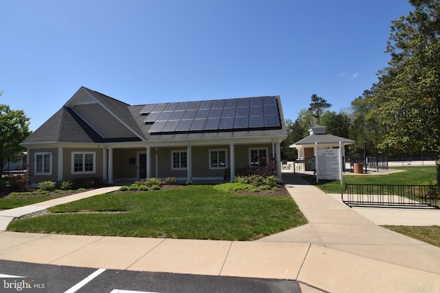 view of front of house with fence, a porch, solar panels, and a front lawn
