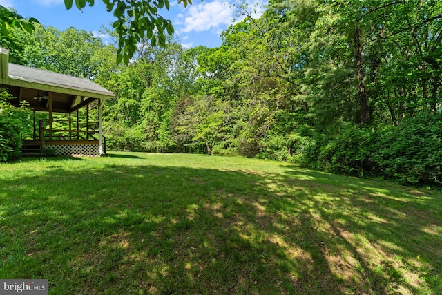 view of grassy yard with a deck, a forest view, and ceiling fan