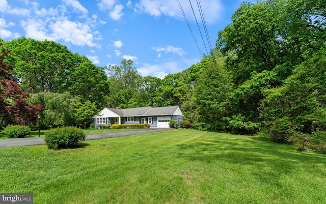 view of grassy yard with asphalt driveway and a garage