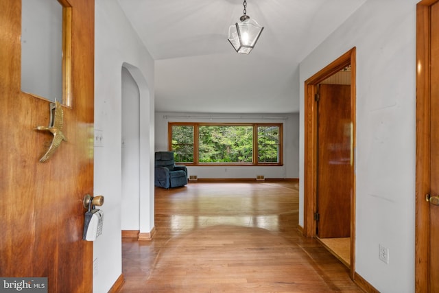 hall featuring arched walkways, wood finished floors, and baseboards