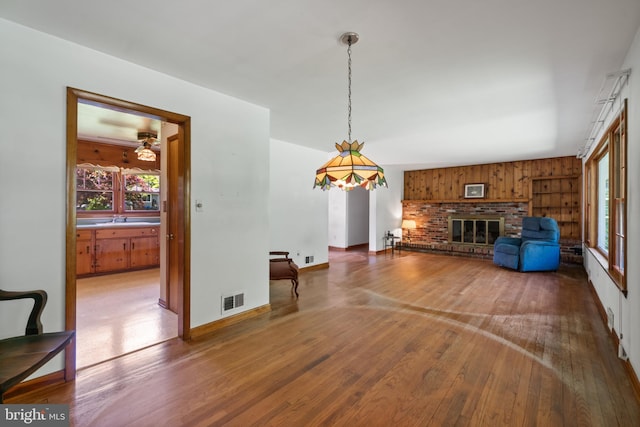 unfurnished living room with wood-type flooring, healthy amount of natural light, a brick fireplace, and baseboards