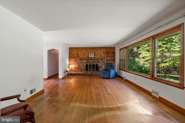 unfurnished living room with arched walkways, baseboards, wood finished floors, and a brick fireplace