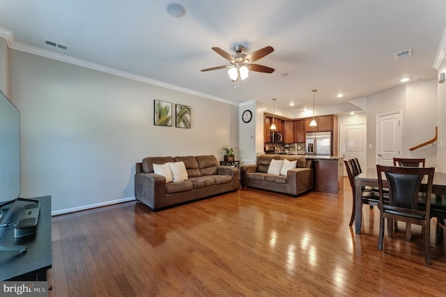 living area with wood-type flooring, ceiling fan, visible vents, and crown molding