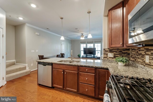 kitchen with light stone countertops, a sink, light wood finished floors, stainless steel appliances, and ornamental molding