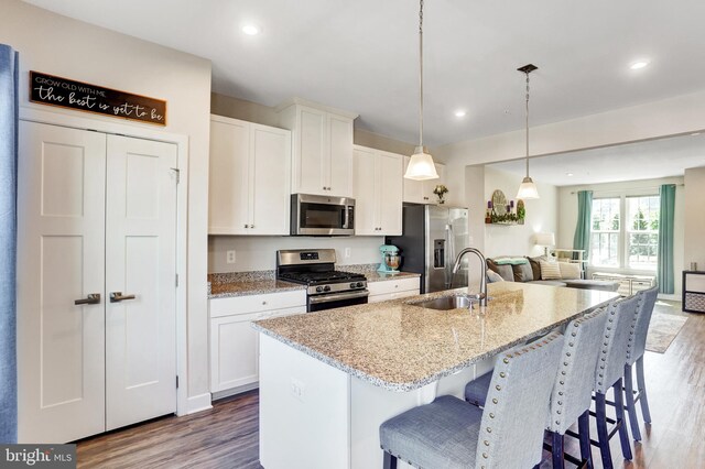 kitchen with appliances with stainless steel finishes, a center island with sink, wood finished floors, a sink, and white cabinetry