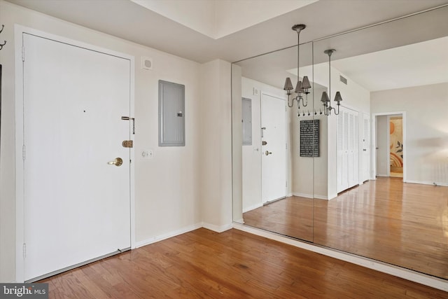 foyer featuring baseboards, electric panel, wood finished floors, and visible vents