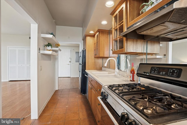 kitchen with brown cabinetry, light countertops, under cabinet range hood, a sink, and stainless steel appliances