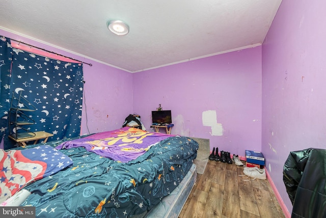 bedroom featuring a textured ceiling, ornamental molding, and wood finished floors