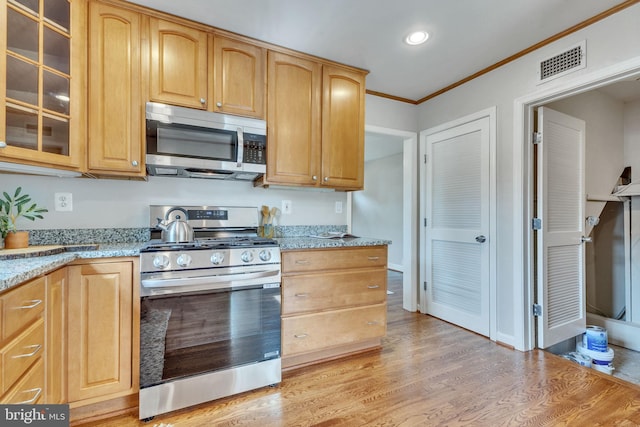 kitchen with stainless steel appliances, ornamental molding, glass insert cabinets, light stone counters, and light wood-type flooring