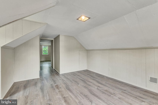 additional living space featuring wood finished floors, vaulted ceiling, and wooden walls