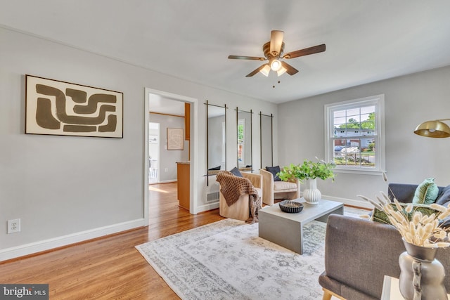 living area with a ceiling fan, wood finished floors, and baseboards