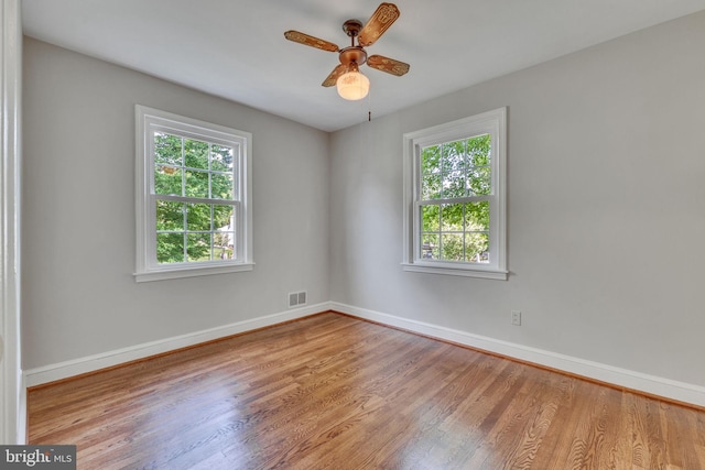 spare room featuring wood finished floors, healthy amount of natural light, baseboards, and a ceiling fan
