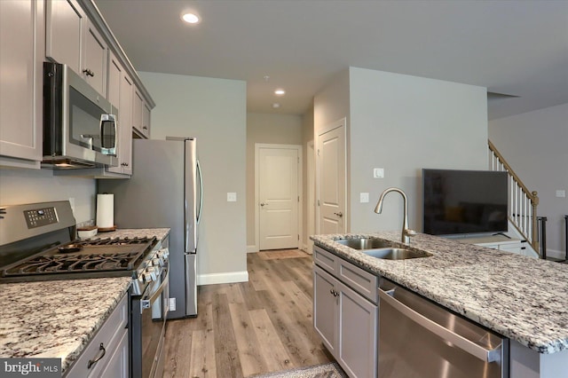 kitchen featuring appliances with stainless steel finishes, a sink, light stone counters, light wood-style floors, and recessed lighting