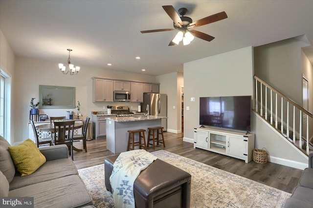 living area featuring stairs, baseboards, ceiling fan with notable chandelier, dark wood-style floors, and recessed lighting