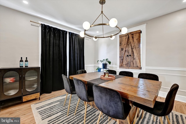 dining area with wainscoting, light wood-type flooring, a notable chandelier, a decorative wall, and recessed lighting