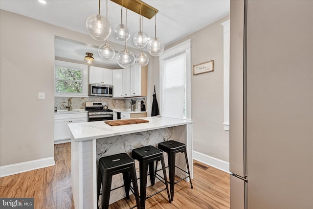 kitchen with baseboards, light wood finished floors, a kitchen bar, and stainless steel appliances