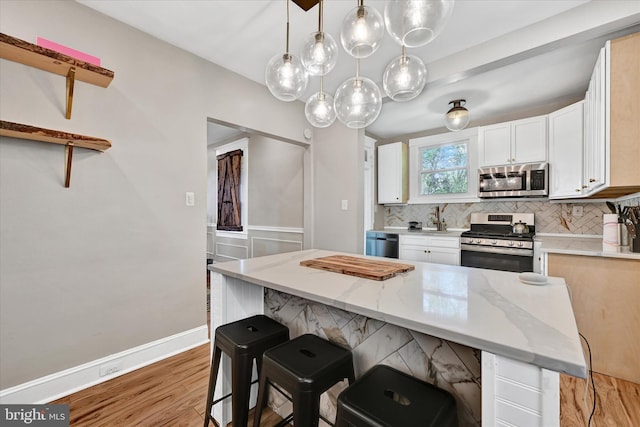 kitchen with light wood-style floors, appliances with stainless steel finishes, decorative backsplash, and white cabinetry