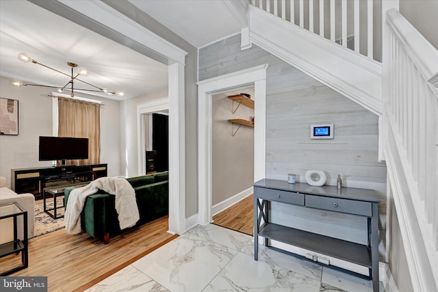 entryway with wooden walls, baseboards, a chandelier, and marble finish floor
