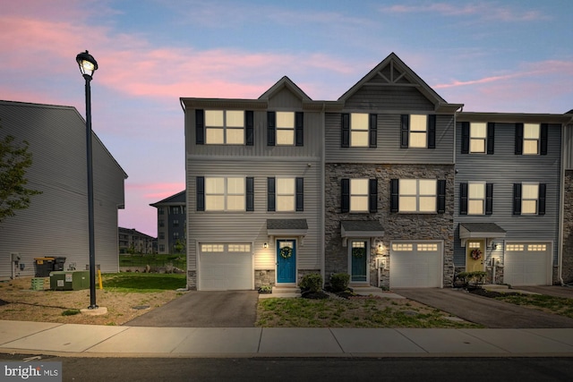 multi unit property featuring driveway, stone siding, and a garage