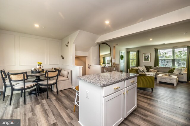 kitchen with a center island, light stone countertops, open floor plan, white cabinetry, and dark wood-type flooring