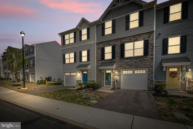 multi unit property with a garage, driveway, and stone siding
