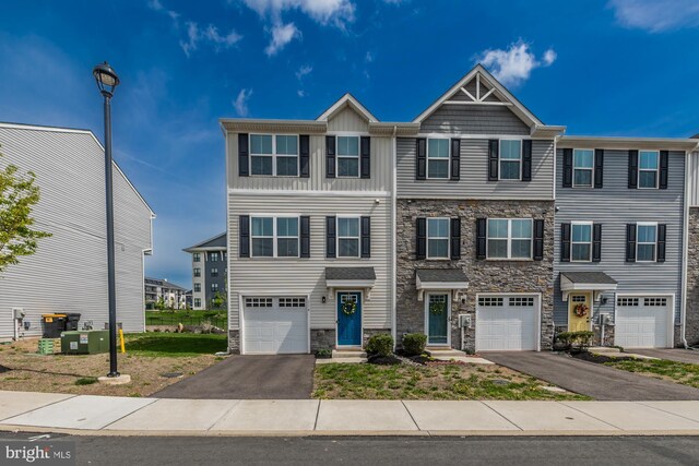 multi unit property with an attached garage, driveway, and stone siding