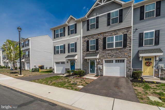 multi unit property featuring an attached garage, a residential view, driveway, and stone siding
