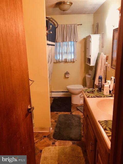 full bathroom with toilet, a shower with curtain, baseboard heating, and vanity