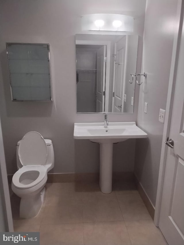 half bath with tile patterned floors, toilet, and baseboards
