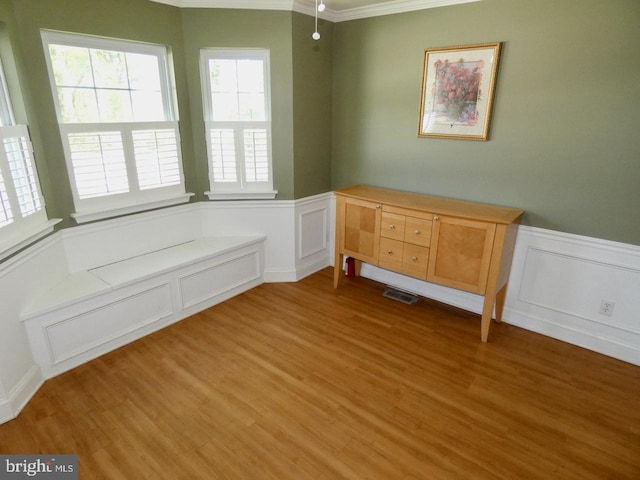 interior space with ornamental molding, wainscoting, a decorative wall, and wood finished floors