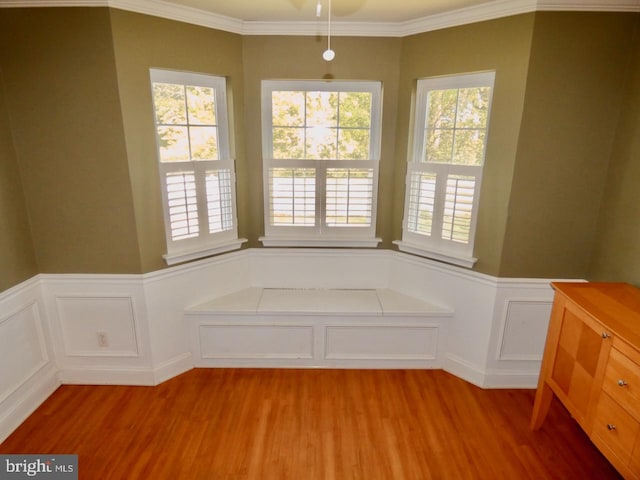 unfurnished dining area featuring ornamental molding, a decorative wall, wood finished floors, and a wainscoted wall