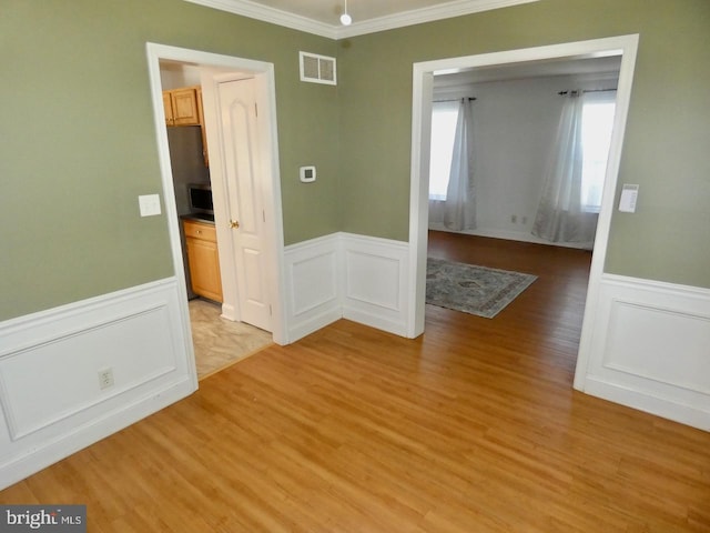 unfurnished room featuring wainscoting, light wood finished floors, a decorative wall, visible vents, and ornamental molding
