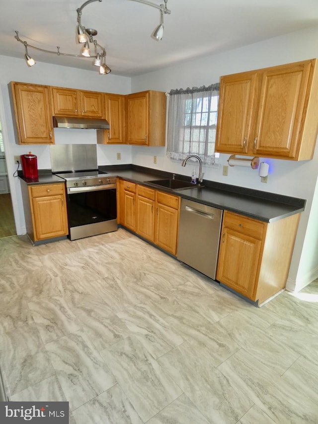 kitchen featuring dark countertops, appliances with stainless steel finishes, a sink, brown cabinetry, and under cabinet range hood